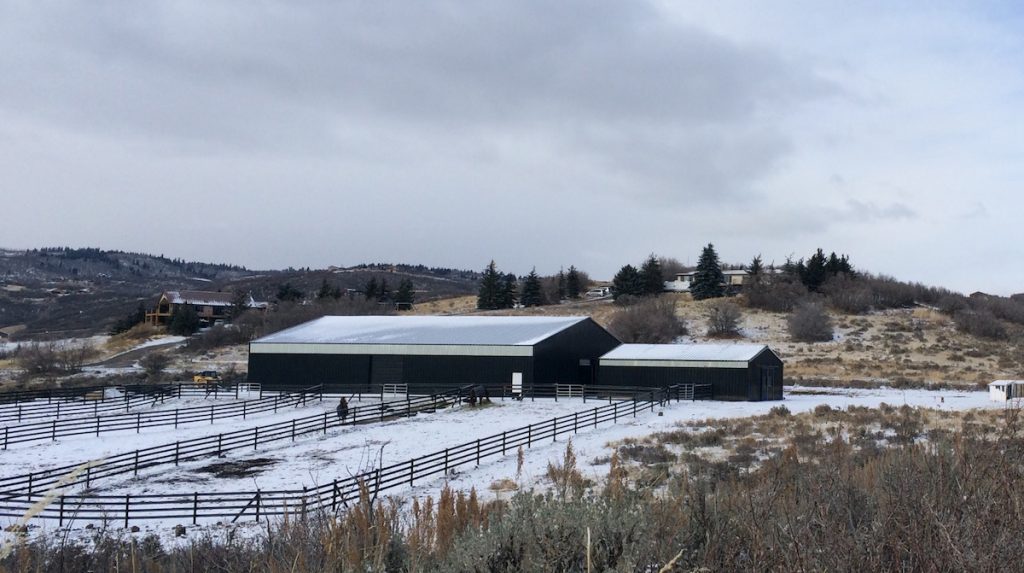 Indoor steel building riding arena in the mountains, covered in snow