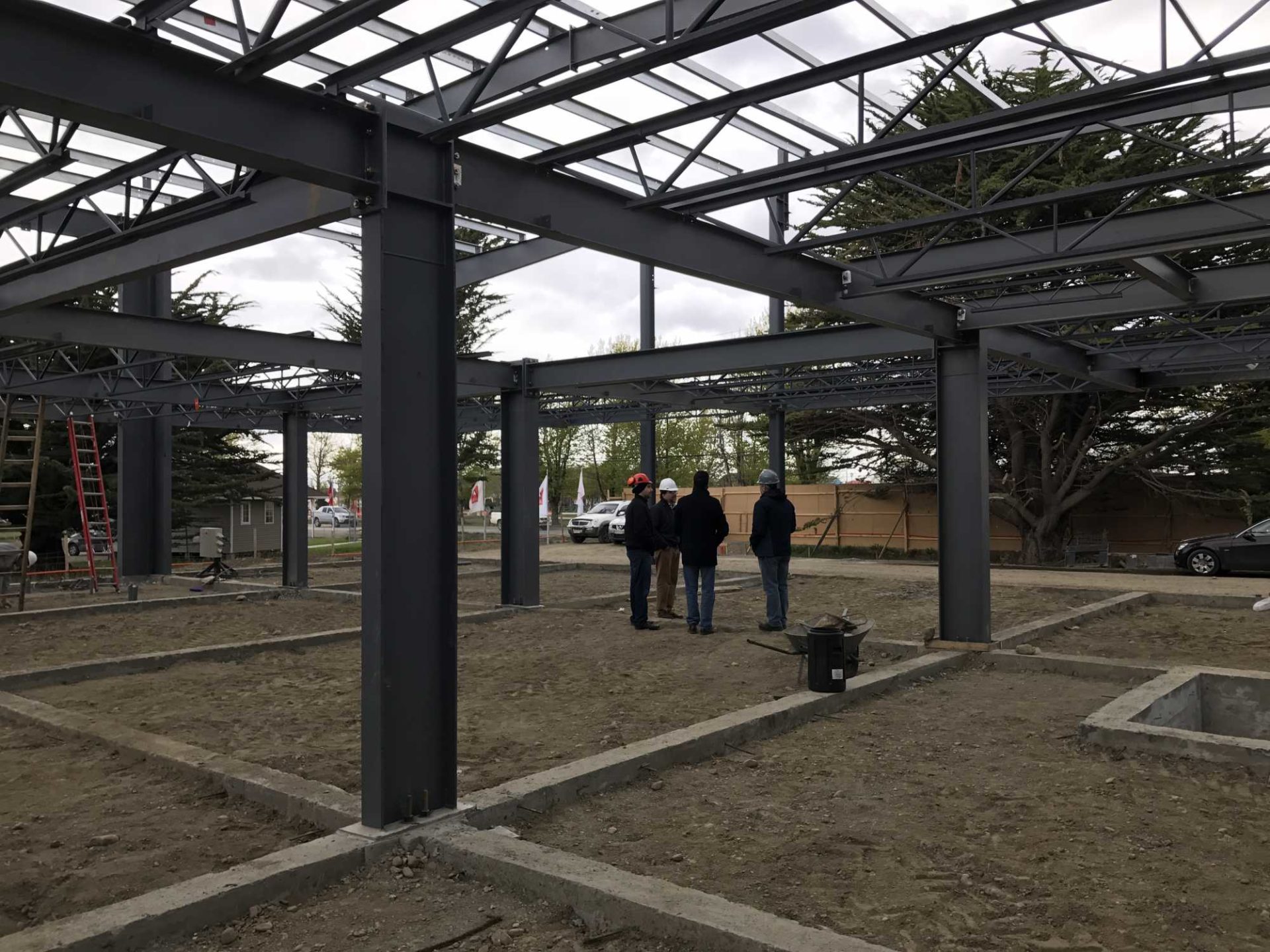 Four builders in hard hats gathered under the structure of a steel building
